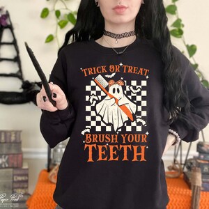 May include: Black sweatshirt with a white ghost holding a toothbrush and the text "Trick or Treat Brush Your Teeth" in orange.
