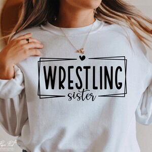 May include: White sweatshirt with black text that reads "WRESTLING sister" in a double-lined box with a small heart above the text.