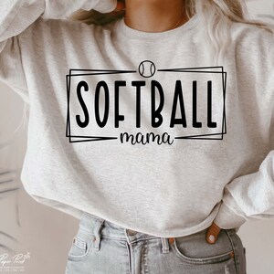 Pu&ograve; includere: Felpa grigio chiaro con la scritta nera "SOFTBALL mama", con una grafica di softball sopra la parola "SOFTBALL". La felpa &egrave; a girocollo.