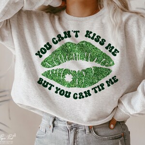May include: A gray sweatshirt with the text "You can't kiss me but you can tip me" in black with a green glitter lip design and a shamrock.