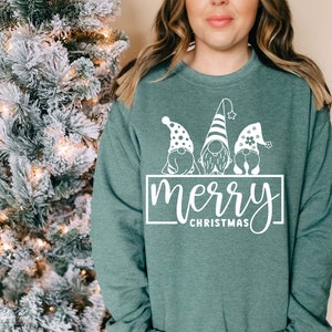 K&ouml;nnte beinhalten: Ein tealgr&uuml;ner Pullover mit einer wei&szlig;en Grafik von drei Gnomen, die H&uuml;te tragen, und dem Text "merry christmas".