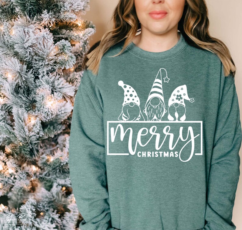 K&ouml;nnte beinhalten: Ein tealgr&uuml;ner Pullover mit einer wei&szlig;en Grafik von drei Gnomen, die H&uuml;te tragen, und dem Text "merry christmas".