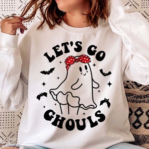 May include: White sweatshirt with a black and white graphic of a ghost wearing a red and white bandana. The text "Let's Go Ghouls" is printed on the sweatshirt.