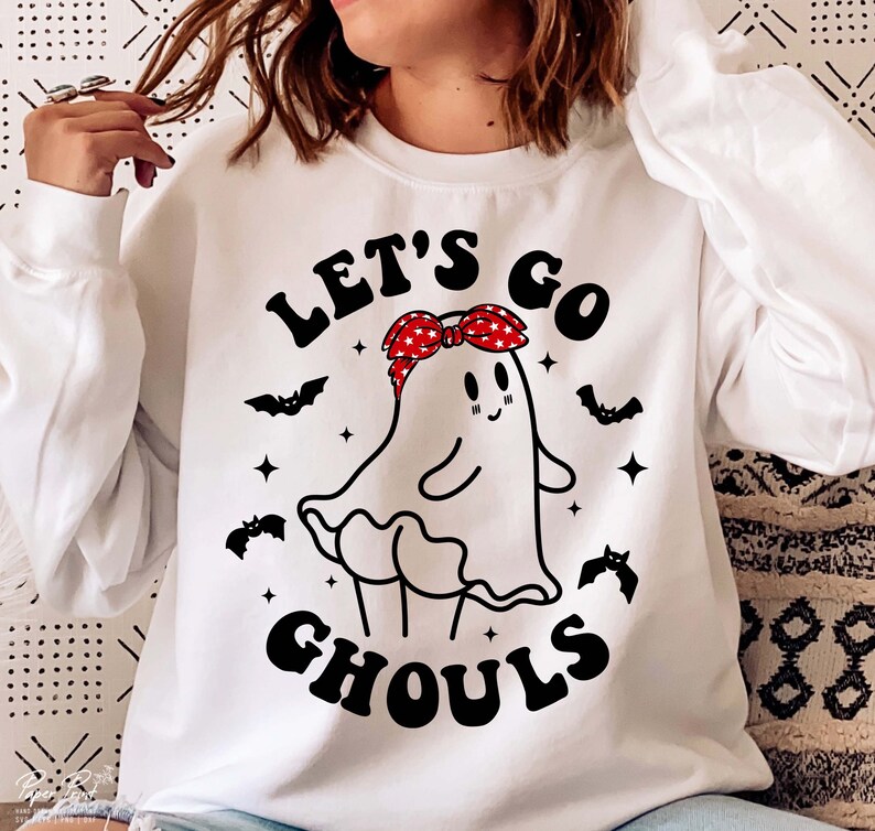 May include: White sweatshirt with a black and white graphic of a ghost wearing a red and white bandana. The text "Let's Go Ghouls" is printed on the sweatshirt.