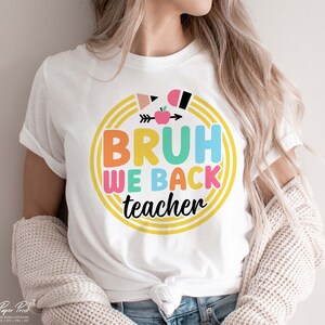 Puede incluir: Camiseta blanca con un dise&ntilde;o circular de colores que dice "Bruh We Back Teacher".