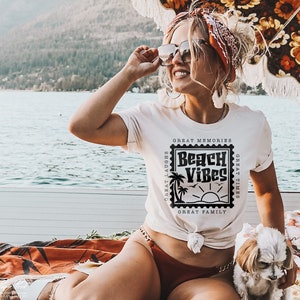 Puede incluir: Una mujer con una camiseta blanca con un gr&aacute;fico negro que dice "Beach Vibes" en un dise&ntilde;o de sello vintage. El gr&aacute;fico tambi&eacute;n incluye palmeras, un sol y el texto "Great Memories, Great Laughs, Great Times, Great Family".