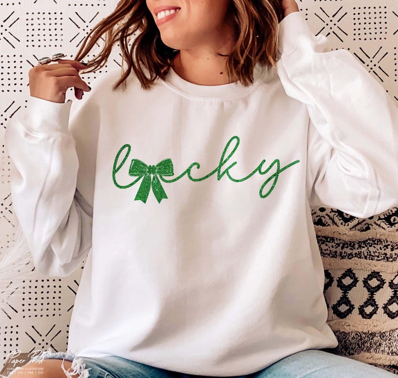 Puede incluir: Sudadera blanca con un dise&ntilde;o de purpurina verde que dice "lucky" con un lazo de purpurina verde.