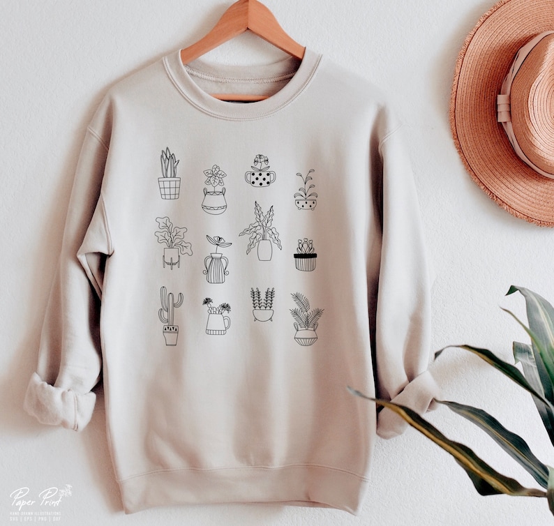 May include: A beige sweatshirt with a black graphic print of various potted plants. The graphic features a variety of plant types, including cacti, succulents, and leafy plants.