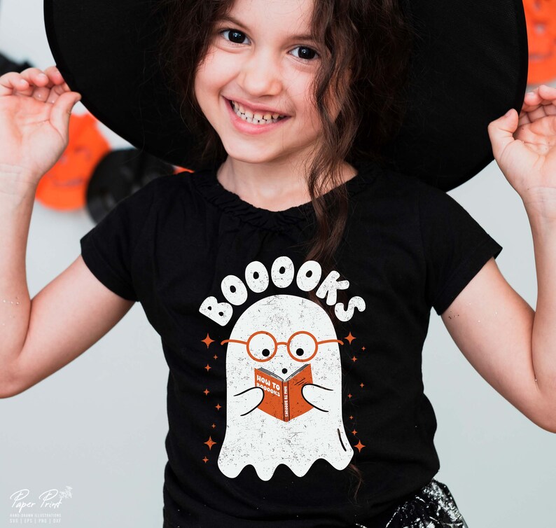 Pode incluir: Uma camiseta preta com um fantasma branco usando &oacute;culos e lendo um livro que diz "How To Boooks". O texto "BOO000KS" est&aacute; acima do fantasma.