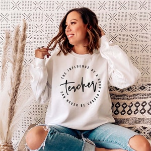 May include: White sweatshirt with a black circle graphic that says "The influence of a good teacher can never be erased".
