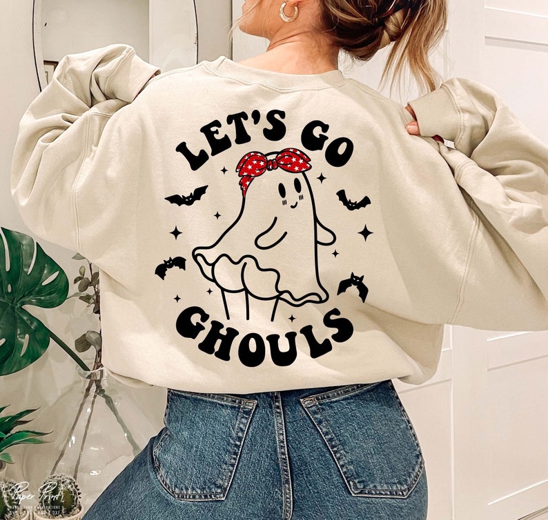 May include: A cream colored sweatshirt with a black and white graphic of a ghost wearing a red bandana. The text "Let's Go Ghouls" is printed on the sweatshirt.