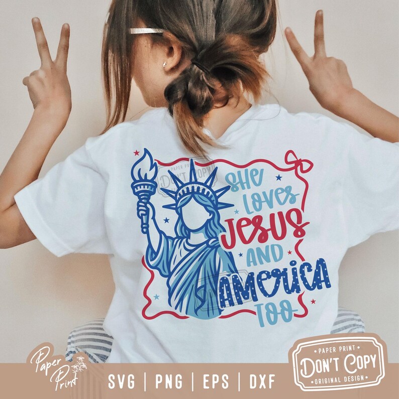 Puede incluir: Una camiseta blanca con un gr&aacute;fico azul y rojo de la Estatua de la Libertad sosteniendo una antorcha. El gr&aacute;fico incluye el texto "She Loves Jesus and America Too".