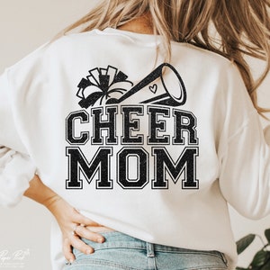 May include: White sweatshirt with black glitter text that reads "Cheer Mom" and a black glitter image of a cheerleader's pom pom and megaphone.