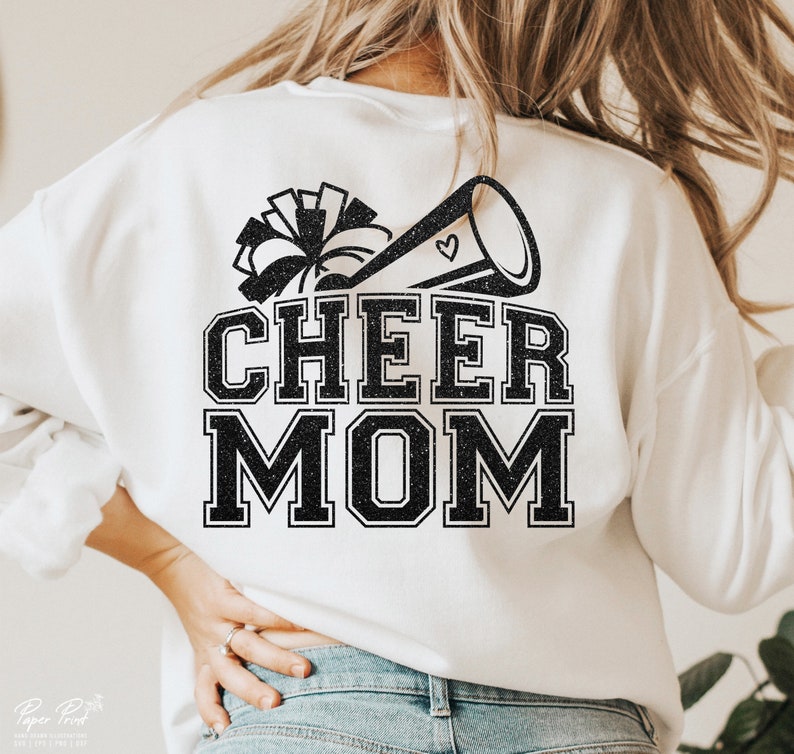 May include: White sweatshirt with black glitter text that reads "Cheer Mom" and a black glitter image of a cheerleader's pom pom and megaphone.