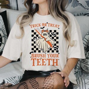 May include: White t-shirt with a graphic of a ghost holding a toothbrush. The text "Trick or Treat Brush Your Teeth" is printed on the shirt.