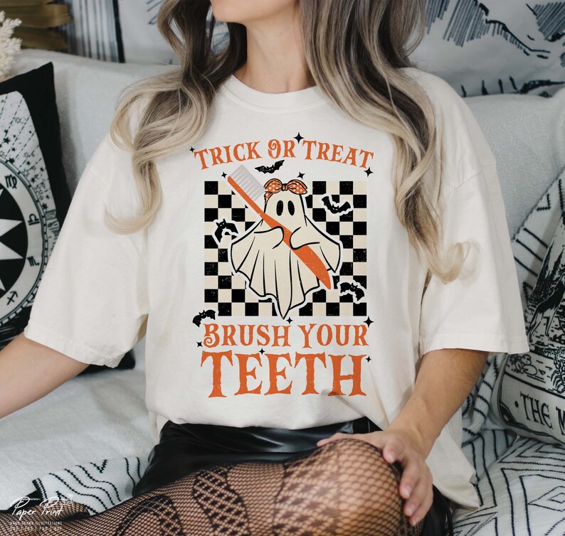 May include: White t-shirt with a graphic of a ghost holding a toothbrush. The text "Trick or Treat Brush Your Teeth" is printed on the shirt.