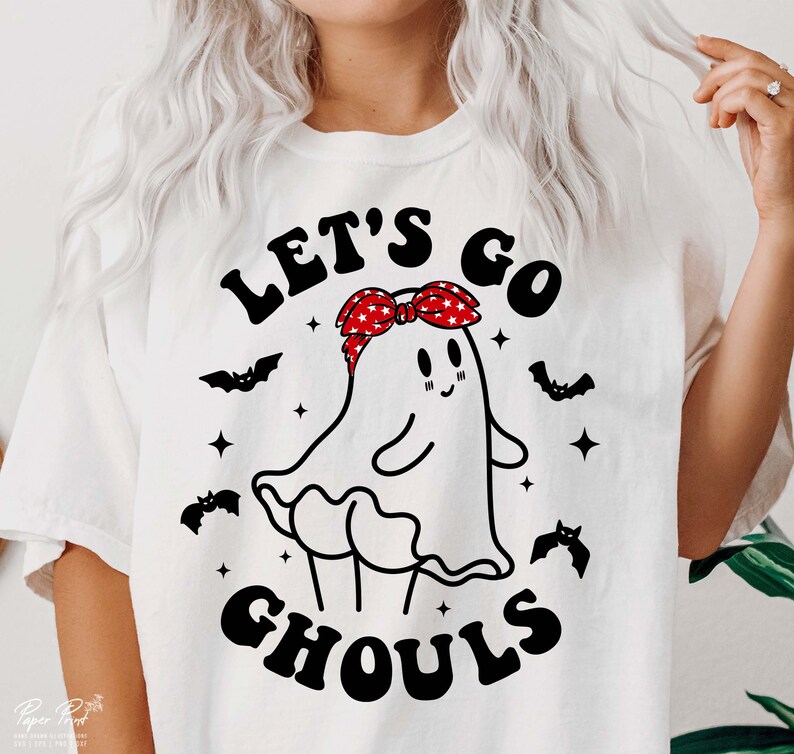 May include: White t-shirt with a black and white illustration of a ghost wearing a red and white bandana. The text "Let's go ghouls" is printed on the shirt.