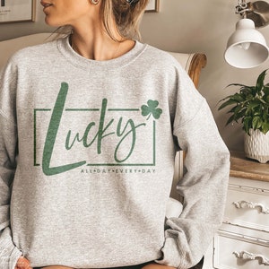 May include: Gray sweatshirt with a green shamrock and the text "Lucky All Day Every Day" in a white box.