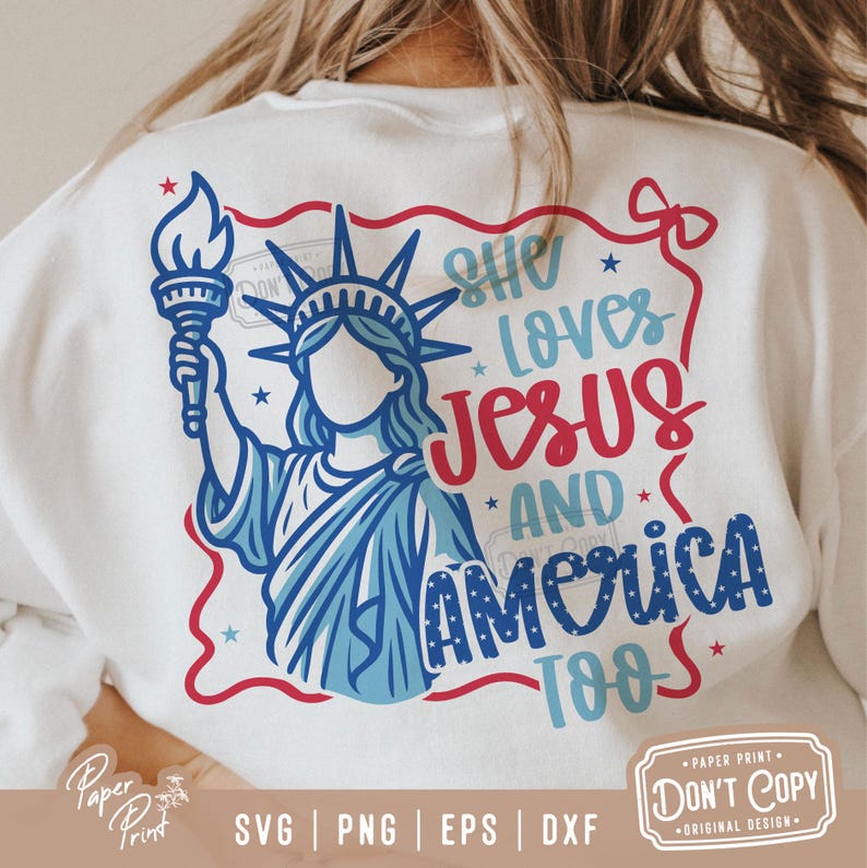 Puede incluir: Una camiseta blanca con un dise&ntilde;o gr&aacute;fico rojo, blanco y azul. El gr&aacute;fico presenta a una mujer vestida como la Estatua de la Libertad sosteniendo una antorcha. El texto "She Loves Jesus And America Too" est&aacute; escrito en letras rojas, blancas y azules.