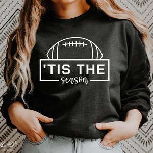 May include: Black sweatshirt with a white outline of a football and the text 'Tis the season'.