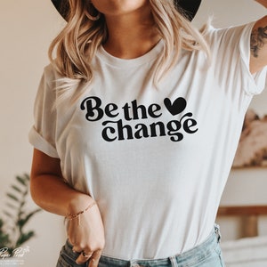 Puede incluir: Camiseta blanca con un gr&aacute;fico negro que dice "Be the &hearts; change" en una fuente retro.