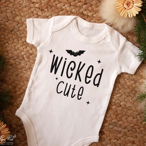 May include: White baby onesie with black text that reads "Wicked cute" and a black bat graphic.
