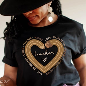 Pu&ograve; includere: Maglietta nera con un design a forma di cuore marrone che presenta una matita e la parola "teacher" all'interno. Il cuore &egrave; circondato dalle parole "Listen, Teacher, Inspire, Love, Motivation, Dream, Connect, Future, Lead, Encourage".