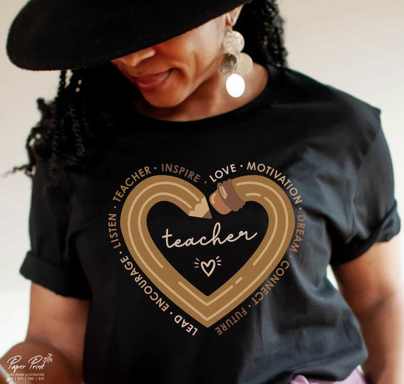 Pu&ograve; includere: Maglietta nera con un design a forma di cuore marrone che presenta una matita e la parola "teacher" all'interno. Il cuore &egrave; circondato dalle parole "Listen, Teacher, Inspire, Love, Motivation, Dream, Connect, Future, Lead, Encourage".
