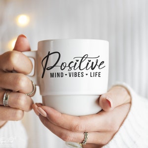 May include: White ceramic mug with black text that reads "Positive Mind Vibes Life" with a heart symbol between each word.