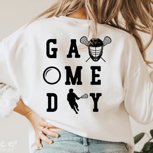 May include: White sweatshirt with black text that reads "Game Day" with a lacrosse stick and helmet graphic.