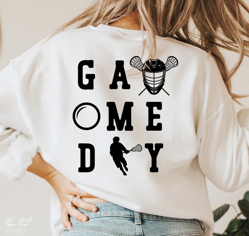 May include: White sweatshirt with black text that reads "Game Day" with a lacrosse stick and helmet graphic.
