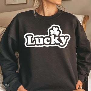May include: Black sweatshirt with a white graphic of a four-leaf clover and the word "Lucky" in a retro font.