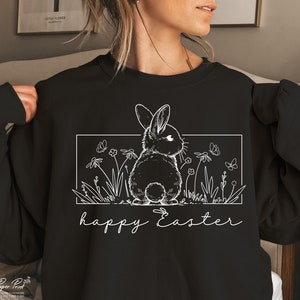 May include: Black sweatshirt featuring a white outline of a rabbit in a field of flowers and butterflies. The text "happy Easter" is written below the image.