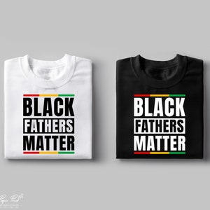 Puede incluir: Dos camisetas con el texto "Black Fathers Matter" en letras negras sobre fondo blanco y fondo negro. El texto est&aacute; enmarcado por una franja roja, amarilla y verde.