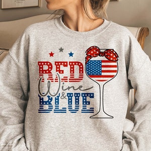 K&ouml;nnte beinhalten: Grauer Pullover mit einem roten, wei&szlig;en und blauen Weinglas-Motiv. Das Glas hat eine rote, wei&szlig;e und blaue Schleife oben und den Text "Red Wine & Blue" in rot, wei&szlig; und blau.