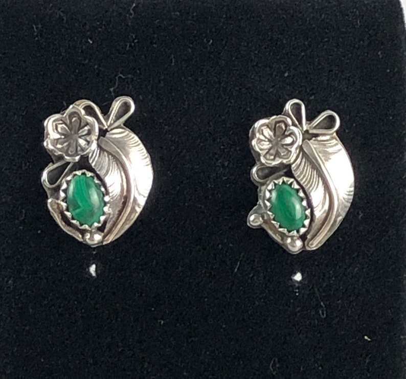 May include: A pair of silver earrings with green malachite stones. The earrings feature a floral design with a feather motif.