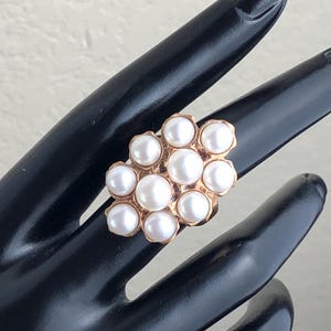 Könnte beinhalten: Ein goldener Ring mit einem Cluster aus weißen Perlen, die in einem blumenartigen Design gesetzt sind.