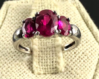 Puede incluir: Un anillo de plata con tres piedras preciosas rojas ovaladas. La piedra central es más grande que las dos laterales. El anillo tiene un diseño clásico con un acabado pulido. Adecuado para uso diario o ocasiones especiales.