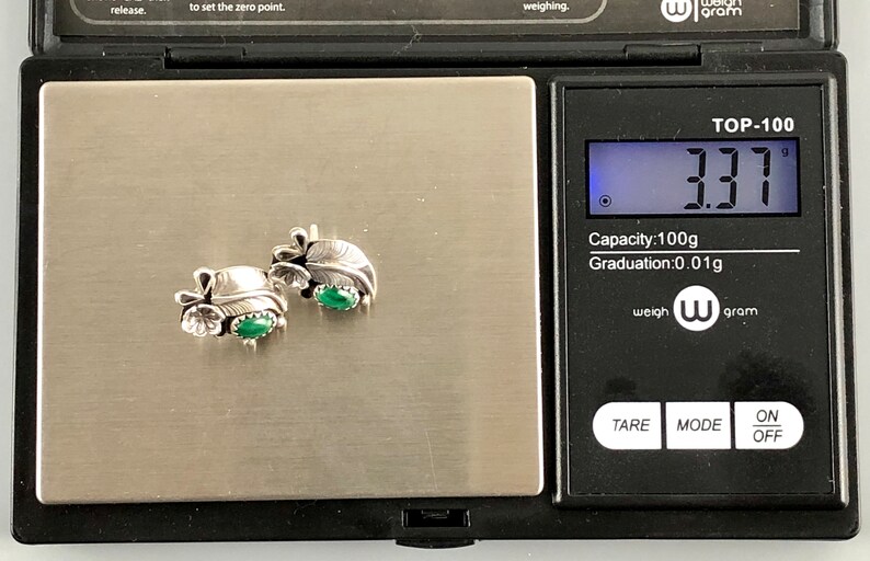 May include: A pair of silver earrings with green stones, weighing 3.31 grams on a digital scale. The scale reads "TOP-100" and has a capacity of 100 grams with a graduation of 0.01 grams.