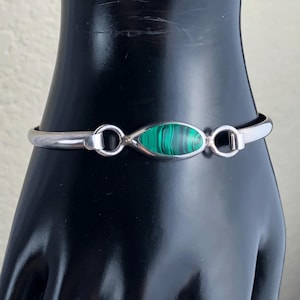May include: A silver bracelet with a green malachite stone set in the centre. The bracelet has two silver rings on either side of the stone.