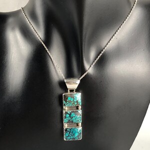 May include: A silver chain necklace with a pendant featuring three turquoise stones set in silver. The stones have a mottled pattern of blue and green.