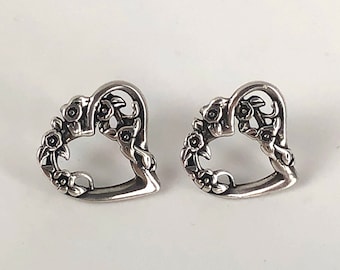 May include: A pair of silver heart-shaped earrings with floral designs. The earrings are made of metal and have a delicate, intricate design.