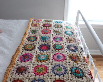 Puede incluir: Una manta de ganchillo con un patrón de cuadrados de la abuela en beige, marrón, rosa, verde, azul y naranja.