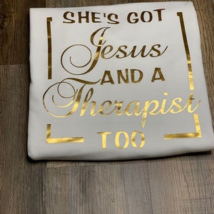 May include: White t-shirt with gold foil lettering that reads "She's got Jesus and a therapist too."