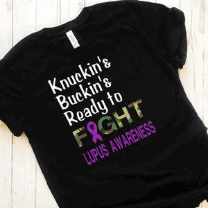 May include: Black t-shirt with a white graphic that says "Knuckin' & Buckin' & Ready to Fight" with a purple ribbon and camouflage pattern. The text "Lupus Awareness" is below the graphic.