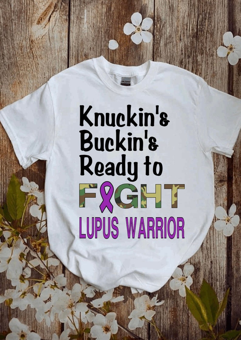 May include: White t-shirt with the text "Knuckin's Buckin's Ready to FIGHT" in black with a purple ribbon and camouflage print. The text "LUPUS WARRIOR" is in purple below the other text.