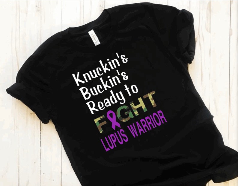 May include: Black t-shirt with a white graphic that reads "Knuckin' & Buckin' & Ready to FIGHT" with a purple ribbon and camouflage pattern. The text "Lupus Warrior" is below the graphic.