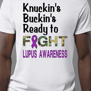 May include: White t-shirt with a purple ribbon and the text "Knuckin's Buckin's Ready to FIGHT LUPUS AWARENESS" in black and green camouflage print.