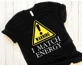 May include: Black t-shirt with a yellow warning sign that says "WARNING" and the text "I MATCH ENERGY" in white.
