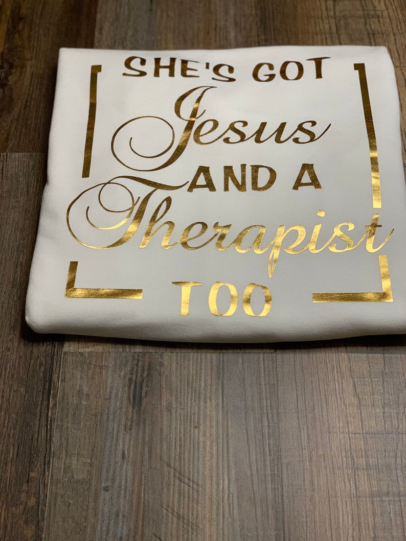 May include: White t-shirt with gold lettering that reads "She's got Jesus and a Therapist too".